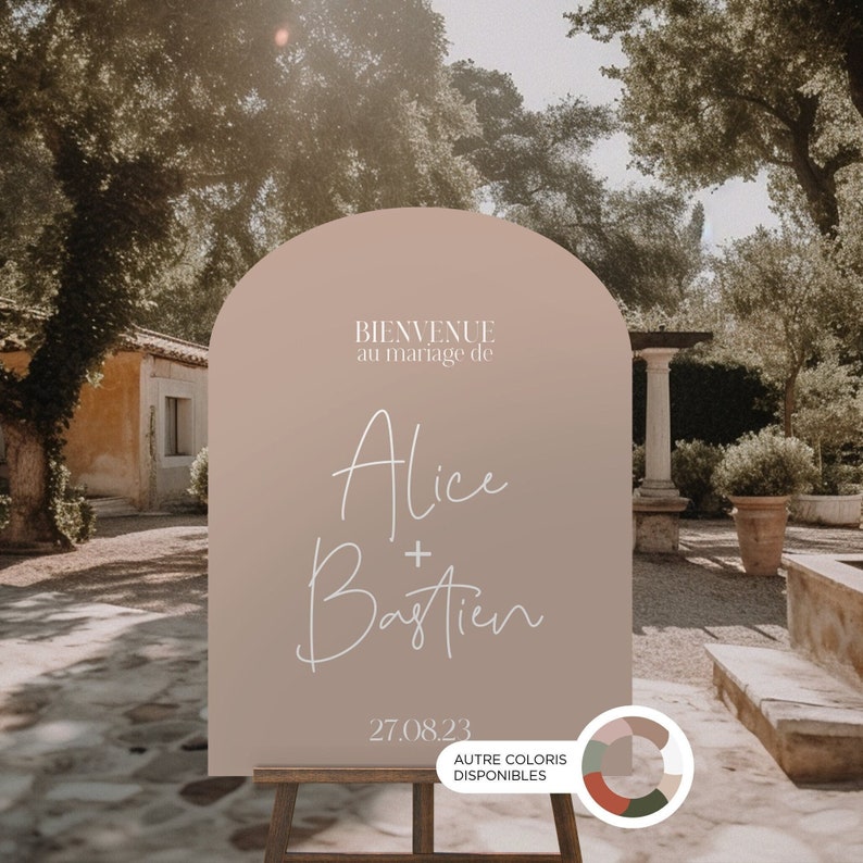 May include: A light brown arch-shaped welcome sign with the text "BIENVENUE au mariage de Alice + Bastien 27.08.23" in white script font. The sign is on a wooden easel and has a color palette sample with the text "AUTRE COLORIS DISPONIBLES".