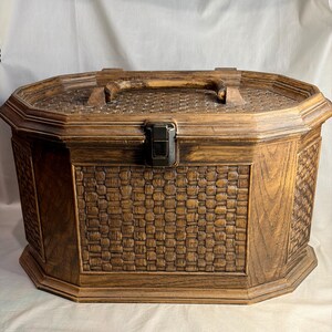 Peut inclure: Coffre de rangement vintage en bois avec un motif de panier tressé sur le devant et les côtés. La boîte a une finition marron foncé, un couvercle à charnière, un fermoir en métal et une poignée en bois. La boîte est de forme octogonale.
