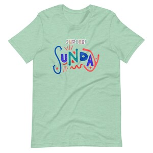 Może przedstawiać: Jasnozielony t-shirt z napisem "SUPERB! SUNDAY" w kolorowych, stylizowanych literach.