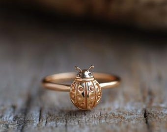 May include: A gold-colored ring featuring a detailed ladybug design. The ladybug has an engraved pattern on its back and small antennae. The ring is set on a thin band, and the overall design is delicate and nature-inspired.