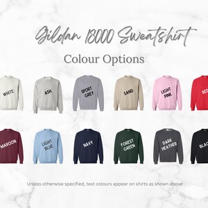May include: A Gildan 18000 sweatshirt is shown in 16 different colors: white, ash, sport grey, sand, light pink, red, maroon, light blue, navy, forest green, dark heather, black.