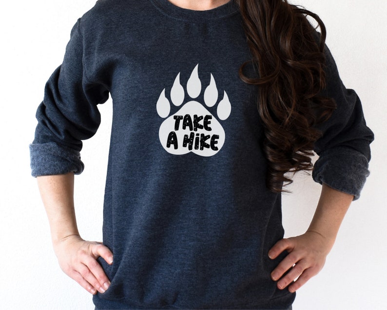 Pode incluir: Uma camisa de moletom azul escura com um gr&aacute;fico de impress&atilde;o de pata de urso branca que diz "Take a Hike".