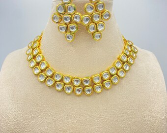 Peut inclure: Un ensemble de collier et boucles d'oreilles en or avec des pierres claires. Le collier a deux rangées de pierres et les boucles d'oreilles sont en forme de goutte.