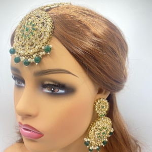 Peut inclure: Une parure de tête de mariée indienne dorée et verte avec un motif rond orné et des perles vertes et blanches pendantes. La parure de tête est portée par un mannequin aux cheveux bruns.