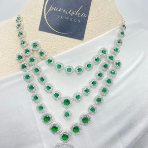 Puede incluir: Un collar de plata de tres niveles con piedras preciosas verdes y un gran colgante. El collar está en un busto de maniquí blanco. El texto "punisha JEWELS" está en una etiqueta negra.
