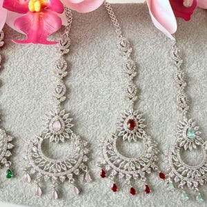 May include: Five silver-toned headpieces with intricate floral and teardrop designs. Each piece features a central gemstone in green, pink, red, and light green, with matching teardrop accents. The headpieces are adorned with clear crystals.