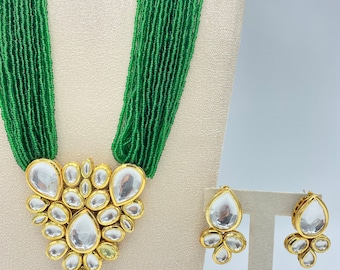 May include: A green beaded necklace with a gold pendant featuring a cluster of clear stones. Matching earrings with a similar design are also included.