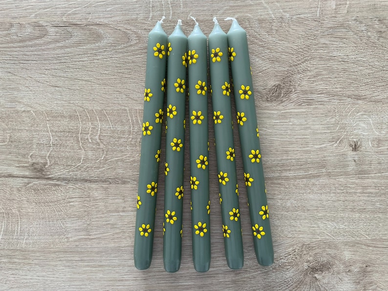 Handbeschilderde kaarsen. Bloemen geschilderde kaarsen. Groene dinerkaarsen met gele zonnebloemen. Gele zonnebloemen met een donkerbruine kern.