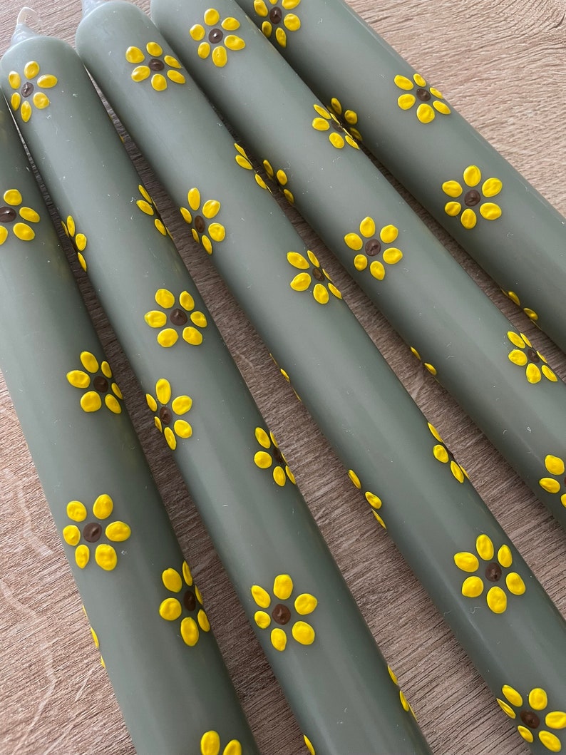 Handbeschilderde kaarsen. Bloemen geschilderde kaarsen. Groene dinerkaarsen met gele zonnebloemen. Gele zonnebloemen met een donkerbruine kern.