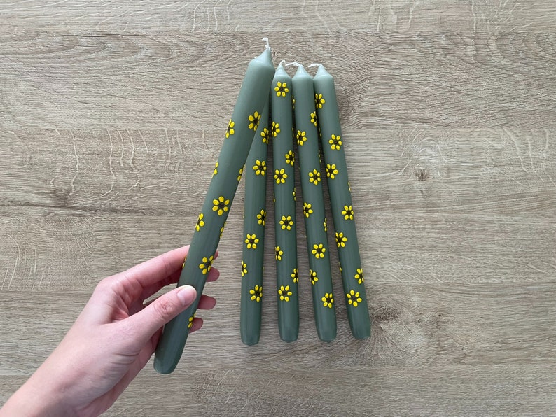 Handbeschilderde kaarsen. Bloemen geschilderde kaarsen. Groene dinerkaarsen met gele zonnebloemen. Gele zonnebloemen met een donkerbruine kern.