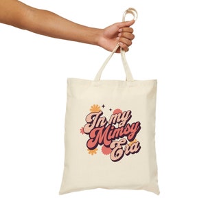 Op de afbeelding: Een beige tote bag met een retro-grafische afbeelding met de tekst "In my Mimsy Era" in roze en oranje letters met bloemmotieven.