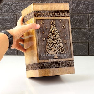 Könnte beinhalten: Eine Holzkiste mit einem geschnitzten Weihnachtsbaumdesign. Die Kiste ist braun und hat einen dunkelbraunen Rand. Der Text "GLOBAL WOOD CRAFT" ist in den Boden der Kiste geschnitzt.