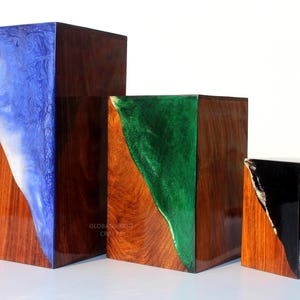 May include: Three wooden blocks with glossy finishes. Each block has a section of colored resin: blue, green, and black. The wood grain is visible, and the blocks vary in size, with the largest on the left.