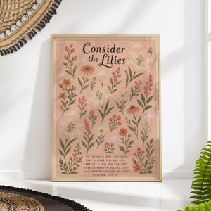 Puede incluir: Un estampado floral enmarcado con el texto "Consider the Lilies". La obra de arte presenta varias flores en tonos blancos, naranjas y rosas sobre un fondo rosa claro. También se incluye la cita de Mateo 6:28-29.