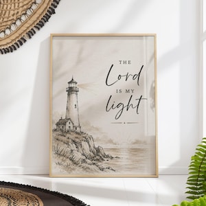 Könnte beinhalten: Ein vertikaler Wandkunstdruck in einem hellen Holzrahmen mit einer sepiafarbenen Illustration eines Leuchtturms auf einer felsigen Klippe über dem Meer. Der Text "THE Lord IS MY light" ist in schwarzer Schreib- und Serifenschrift abgebildet.