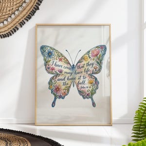 May include: A framed watercolour print depicting a butterfly with floral patterns in blue, pink, and yellow. The butterfly wings contain the text "I have come that they may have life, and have it to the full. John 10:10."