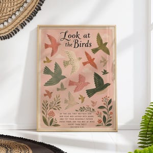 Può includere: Stampa artistica incorniciata con sfondo rosa, raffigurante uccelli colorati in volo. Il testo "Look at the Birds" è in alto, seguito da un versetto biblico. Gli uccelli sono rosa, verdi e bianchi.