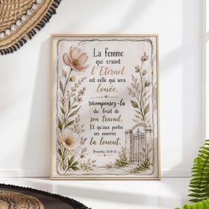 Op de afbeelding: Een ingelijste print met Franse tekst en bloemenillustraties. De tekst luidt: "La femme qui craint l'Eternel est celle qui sera louée." Het kunstwerk toont een poort en botanische elementen in zachte kleuren.