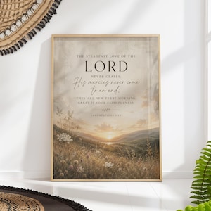 Puede incluir: Una impresión enmarcada con una escena de paisaje y una puesta de sol sobre un campo de flores silvestres. El texto dice: "El amor constante del Señor nunca cesa; sus misericordias nunca terminan". La impresión está en un marco de madera.