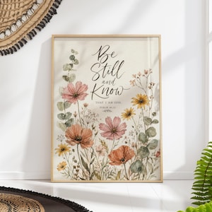 Peut inclure: Une impression encadrée à l'aquarelle avec le texte "Be Still and Know" et des illustrations florales. L'œuvre présente des fleurs roses, oranges et jaunes, avec un feuillage vert. Le cadre est de couleur bois clair.