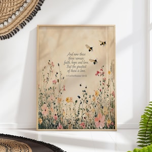 Puede incluir: Una impresión enmarcada que representa un prado floral con abejas. La obra de arte incluye el texto "And now these three remain: faith, hope and love. But the greatest of these is love. 1 Corinthians 13:13."
