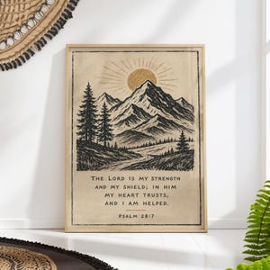 May include: A rectangular wall art print in a light wood frame featuring a black ink illustration of a mountain range, pine trees, and a golden sun. The text reads: THE LORD IS MY STRENGTH AND MY SHIELD; IN HIM MY HEART TRUSTS, AND I AM HELPED. PSALM 28:7.