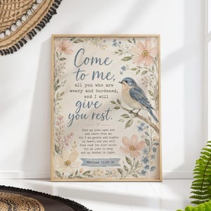 Könnte beinhalten: Gerahmter Kunstdruck mit hellem Holzrahmen. Das Kunstwerk zeigt einen blauen Vogel auf einem Ast, umgeben von floralen Elementen in sanften Pastellfarben. Der Text lautet: „Kommt her zu mir, alle, die ihr mühselig und beladen seid, ich will euch erquicken."