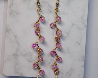 May include: A pair of long, dangling earrings with a gold wire design and pink and clear glass beads.
