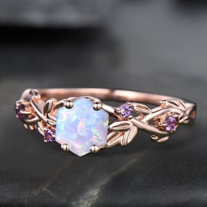May include: A rose gold ring with a white opal gemstone surrounded by a delicate vine design with small pink gemstones.
