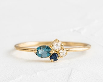 May include: A gold ring with a cluster of blue and white gemstones. The ring features a larger oval-shaped blue gemstone, a smaller round blue gemstone, and two smaller round white gemstones.