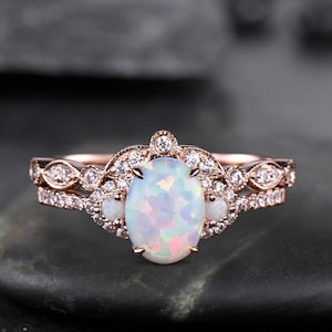 May include: A rose gold engagement ring set with a large oval opal surrounded by smaller diamonds. The ring has a delicate, vintage-inspired design.