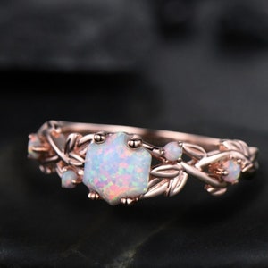 May include: A rose gold ring with a white opal gemstone surrounded by delicate leaf details. The ring is set with smaller white opals on the band.