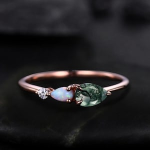 May include: A delicate rose gold ring with three stones: a small clear diamond, a white opal, and a pear-shaped green moss agate.