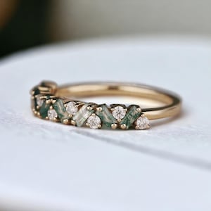 May include: A gold band ring with a chevron pattern of green and clear gemstones.