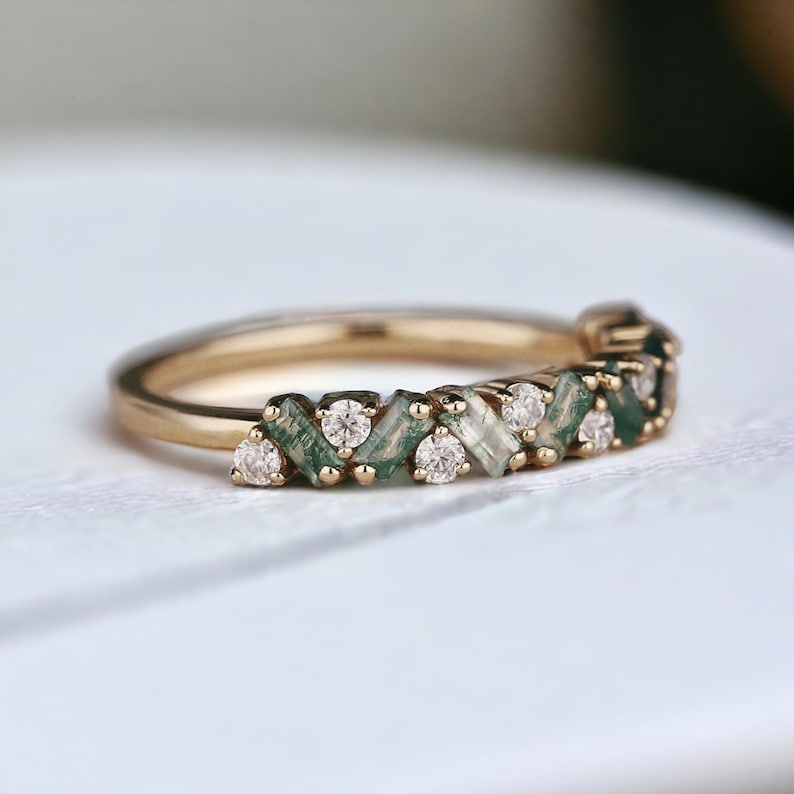 May include: A gold band ring with a row of alternating green and white gemstones. The green gemstones are baguette-shaped and the white gemstones are round.