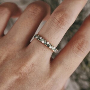 May include: A gold band ring with a row of alternating green and white gemstones.