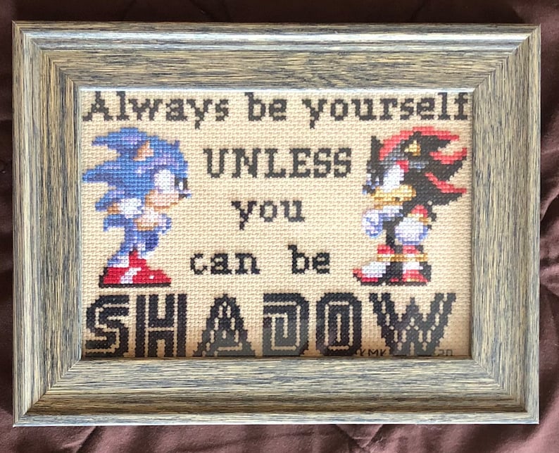 Op de afbeelding: Een ingelijst kruissteekwerk met de videogamepersonages Sonic the Hedgehog en Shadow the Hedgehog. Het kruissteekwerk luidt "Always be yourself unless you can be SHADOW".