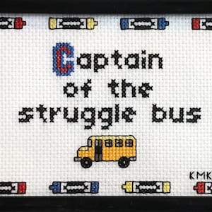 Peut inclure: Broderie encadrée avec l'inscription "Captain of the struggle bus". Le motif comprend un bus scolaire jaune et des illustrations de crayons. Le texte et les images sont brodés en noir, rouge, bleu et jaune sur fond blanc.