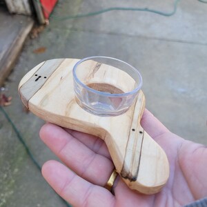 May include: A wooden shot glass holder shaped like a cartoon face with a small, clear glass shot glass resting in the holder.