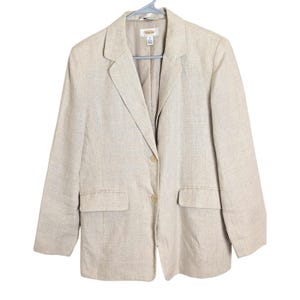 以下が含まれることがあります： 2つのフロントポケットと2つボタンの留め具が付いた、明るいベージュのブレザー。 ブレザーはグレーのハンガーに吊るされています。 Talbotsブランドのラベルが内側に表示されています。 ブレザーはテクスチャード加工された生地で作られています。