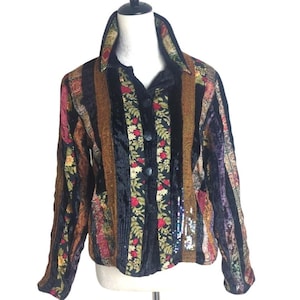 Könnte beinhalten: Eine langärmelige Knopfjacke mit einem Patchwork-Design aus schwarzem Samt, Blumenmustern mit roten und gelben Blüten, braunen strukturierten Einsätzen und Abschnitten mit silbernen Pailletten. Die Jacke hat einen strukturierten Kragen.