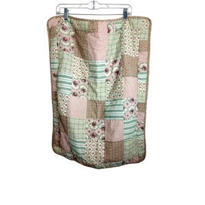 May include: A rectangular patchwork quilt featuring a variety of fabric squares in shades of sage green, soft pink, and tan. The patterns include floral prints, small red and white gingham checks, and green and white stripes, all bordered by a tan trim.
