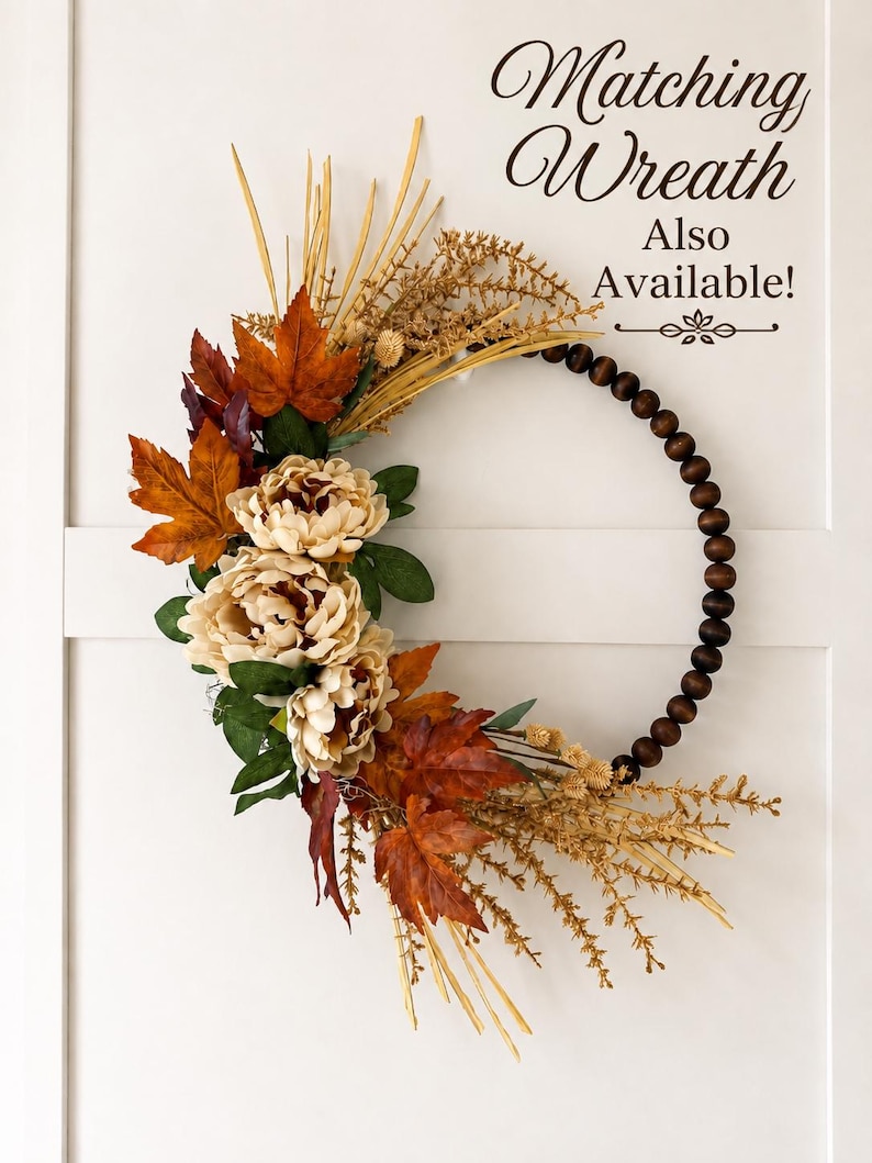 May include: A circular wreath featuring dark brown wooden beads on one side and a cluster of cream-colored peonies, orange and red maple leaves, and dried grasses on the other. The text "Matching Wreath Also Available!" is printed in the upper right.