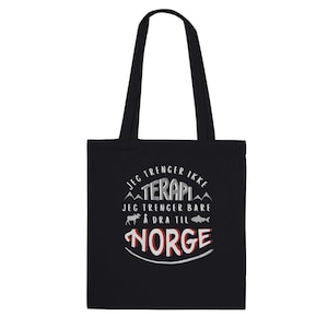 May include: Black tote bag with white text that reads "Jeg trenger ikke terapi, jeg trenger bare å dra til Norge". The text is surrounded by a mountain range graphic and a moose and fish icon.