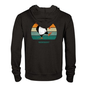 Può includere: Felpa con cappuccio nera con una grafica retrò di un pulcinella di mare in piedi su uno sfondo di tramonto. La grafica include la parola "NORWAY" sotto il pulcinella di mare.