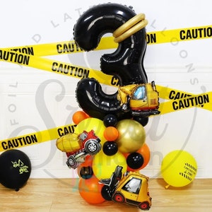May include: A celebratory balloon display with a large black number 3, gold detailing, and construction-themed balloons. Includes a yellow excavator, cement truck, and forklift balloons, plus yellow and orange balloons. Yellow caution tape with the word "CAUTION" is also present.