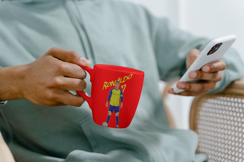 Puede incluir: Una taza de cer&aacute;mica roja con un gr&aacute;fico de un jugador de f&uacute;tbol y el texto "RONALDO 7".