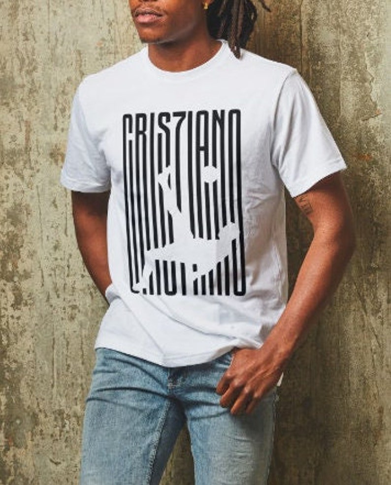 May include: White t-shirt with a black and white graphic print of the word "Cristiano" with a stylized image of a soccer player.
