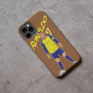 Puede incluir: Una funda de tel&eacute;fono marr&oacute;n con una ilustraci&oacute;n amarilla y azul de un jugador de f&uacute;tbol con el texto "Ronaldo 7" en la funda.