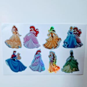 Könnte beinhalten: Eine Blatt mit bunten Prinzessinnen-Stickern mit Disney-Prinzessinnen wie Belle, Arielle, Cinderella und vielen mehr. Die Sticker sind holografisch und haben einen glänzenden Überzug.